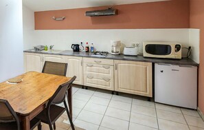 Eine kleine Küche mit Holztisch, Schränken, einer Mikrowelle, einer Kaffeemaschine und einem Kühlschrank.