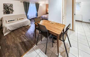 Ein Zimmer mit einem Bett, einem Holztisch mit Stühlen, einer Zimmerpflanze und einem Fenster mit Vorhängen.