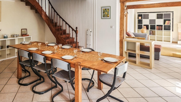 A dining area with a wooden table set for six, a staircase, and a bookshelf with books and decorative items. - Charmante maison avec piscine (Saint-Simon-de-Bordes)
