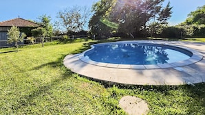 A swimming pool with a curved edge, surrounded by a grassy lawn and trees. - Charmante maison avec piscine (Saint-Simon-de-Bordes)