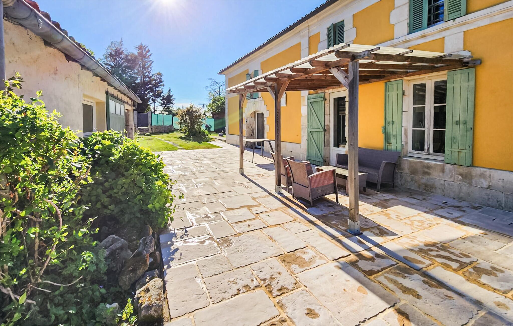 Une cour avec un sol en pierre, des sièges extérieurs et une structure en forme de pergola.
