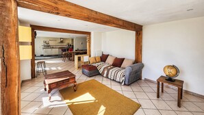 A living room with a sofa, a coffee table, and a rug. There is a kitchen in the background. - Charmante maison avec piscine (Saint-Simon-de-Bordes)