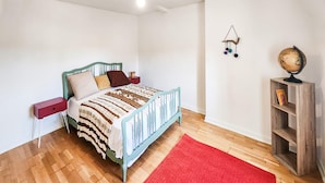 A bedroom with a bed, a red rug, a wooden nightstand, a wooden shelf with a globe, and a wall hanging. - Charmante maison avec piscine (Saint-Simon-de-Bordes)