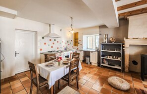 Uma cozinha com mesa de jantar, cadeiras, fogão e prateleira com utensílios de cozinha.