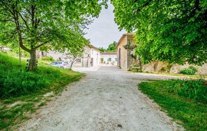 A rural road leading to a row of traditional buildings with a dirt path and greenery on either side. - harmant gîte au calme (Saint-Maigrin)