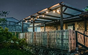 A rustic building with a stone wall, a wooden fence, and a covered outdoor area with string lights. - harmant gîte au calme (Saint-Maigrin)