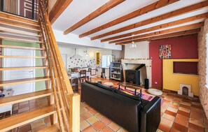 A spacious living area with a fireplace, wooden beams, a staircase, and a kitchen in the background. - harmant gîte au calme (Saint-Maigrin)