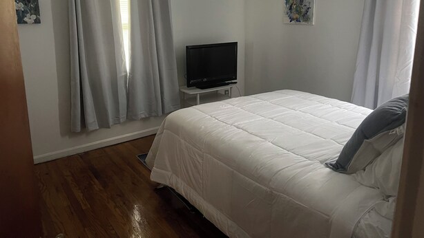 Een slaapkamer met een bed, een televisie op een standaard en twee schilderijen aan de muur.