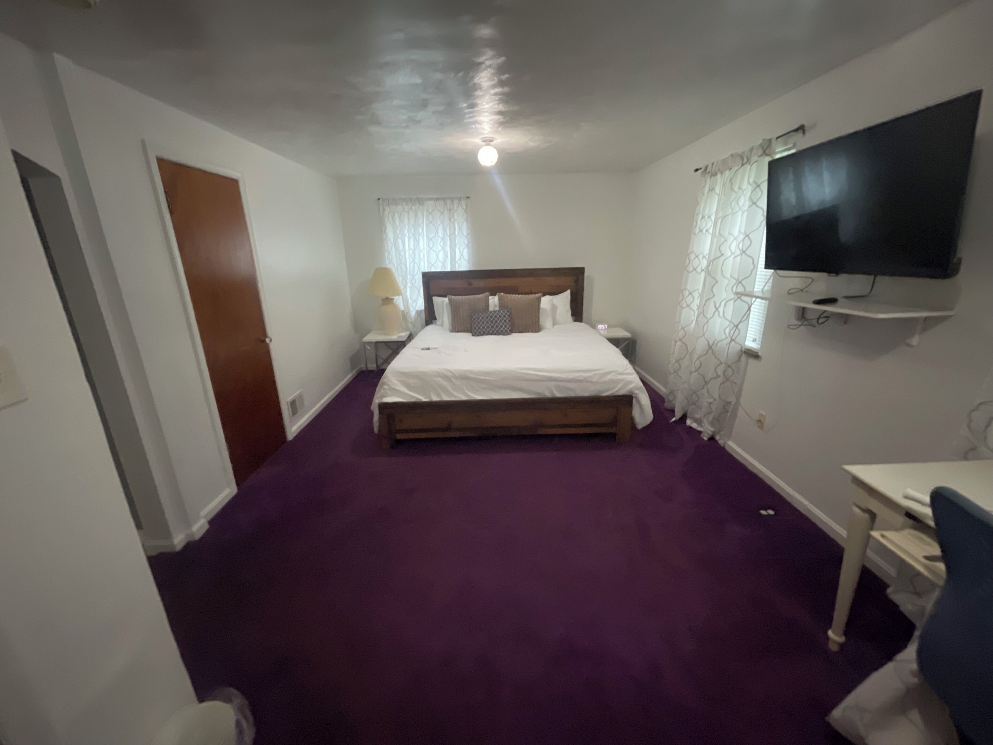 Ein Hotelzimmer mit Bett, Schreibtisch, Fernseher und einem Fenster mit Vorhängen.