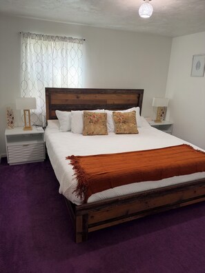 A bedroom with a wooden bed, white bedding, a purple carpet, and two bedside tables with lamps. - Relaxing 2BR Apartment Near UC & Downtown (Cincinnati)