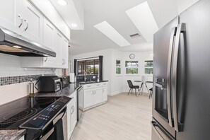 A modern kitchen with white cabinetry, a black induction cooktop, and a stainless steel refrigerator. - Waterfront - Heated Pool - Dock - Gulf Access - Bring Your Boat (Port Charlotte)