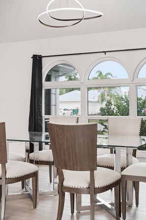 A dining area with a glass table, wooden chairs, and a view through large windows. - Waterfront - Heated Pool - Dock - Gulf Access - Bring Your Boat (Port Charlotte)