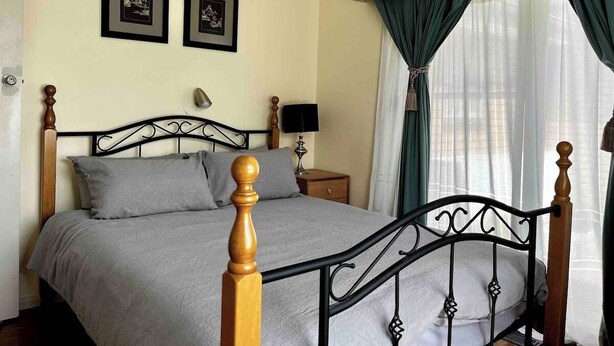 A neatly made bed with a headboard, a bedside table with a lamp, and two framed pictures on the wall. - Ringwood 4BR House near Eastland + Parking (Ringwood)
