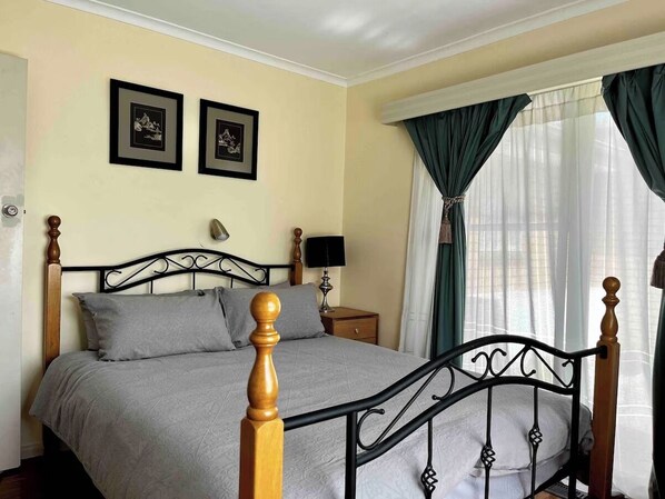 A neatly made bed with a headboard, a bedside table with a lamp, and two framed pictures on the wall.