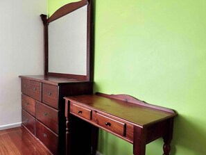 A wooden dresser with drawers and a mirror, against a green wall.