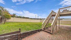 A backyard with a wooden staircase leading to a deck, surrounded by a fence and a grassy lawn. - Callow Place 10 - town location, relaxation, easy coastal living, Wifi (Bermagui)