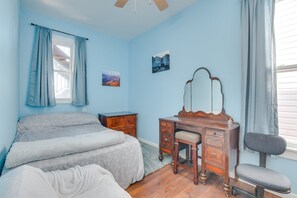 Ein Schlafzimmer mit einem Bett, einem Schminktisch mit Spiegel, einem Sessel und einem Fenster mit Vorhängen.