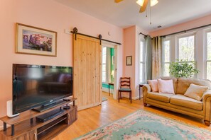A living room with a flat-screen TV, a sofa, a wooden door, and a window with curtains. - Spacious 3-bedroom apartment in brilliant Chicago with AC Logan Square area, (Chicago)