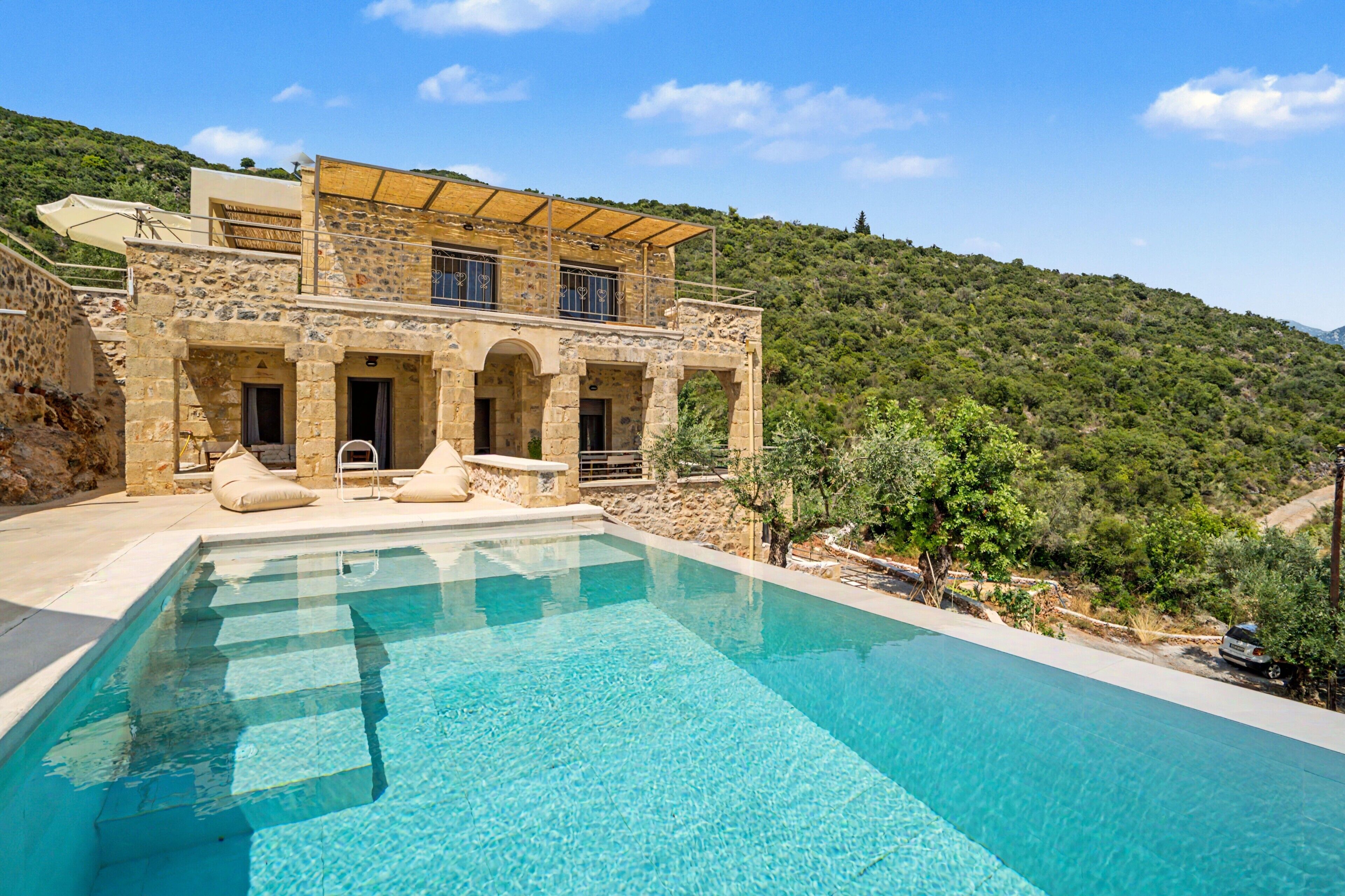 A stone villa with a swimming pool, a covered outdoor area, and a hillside backdrop.