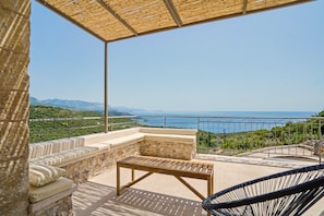 A terrace with a wooden table and chairs, overlooking a coastal landscape with mountains and the sea. - Isichia Apartment with Sea and Taygetos Mountain Views (West Mani)