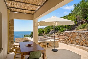 Eine Terrass mit Tisch und Stühlen, einer Steinmauer und Blick aufs Meer.