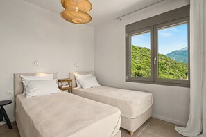 Una camera da letto con due letti, una finestra vista su del verde e una lampada del soffitto in fibra naturale.
