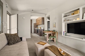 Een moderne woonkamer met een bank, een salontafel en een aan de muur bevestigde televisie. Er is een eethoek met een tafel en stoelen.