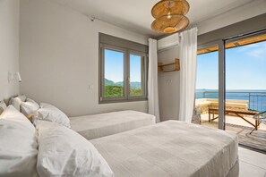 Ein Schlafzimmer mit zwei Betten, einem großen Fenster und einem Balkon mit Meerblick.
