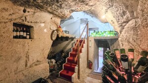 Una bodega subterránea con paredes de piedra, una escalera alfombrada de color rojo y botellas de vino dispuestas en estanterías.