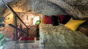 Una habitación tipo cueva con una cama, almohadas y una escalera que lleva a otra zona.