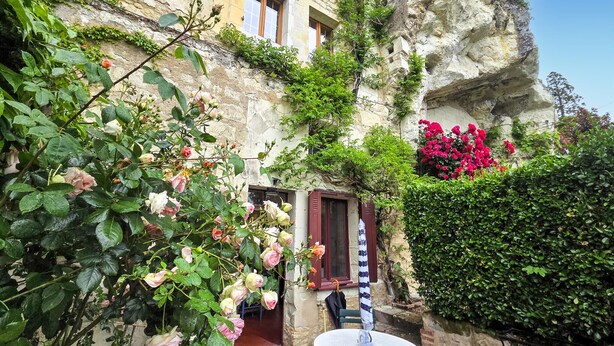 Un edificio de piedra con jardín, una mesa con sombrilla y diversas flores.