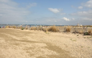 A sandy beach with a wooden fence, people, and boats in the distance. - 1 bedroom beautiful apartment in Le Grau-du-Roi (Le Grau-du-Roi)