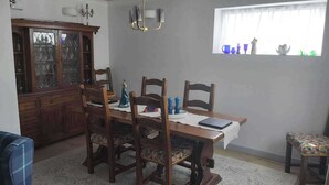 Un comedor con una mesa de madera, cuatro sillas, una araña, un ventanal con adornos y un aparador.