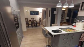 Una cocina moderna con armarios grises, una isla central, luces colgantes y un comedor con mesa y sillas.