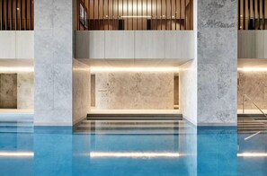 Ein moderner Poolbereich im Innenbereich mit Marmorwänden und einem klaren, blauen Schwimmbecken.