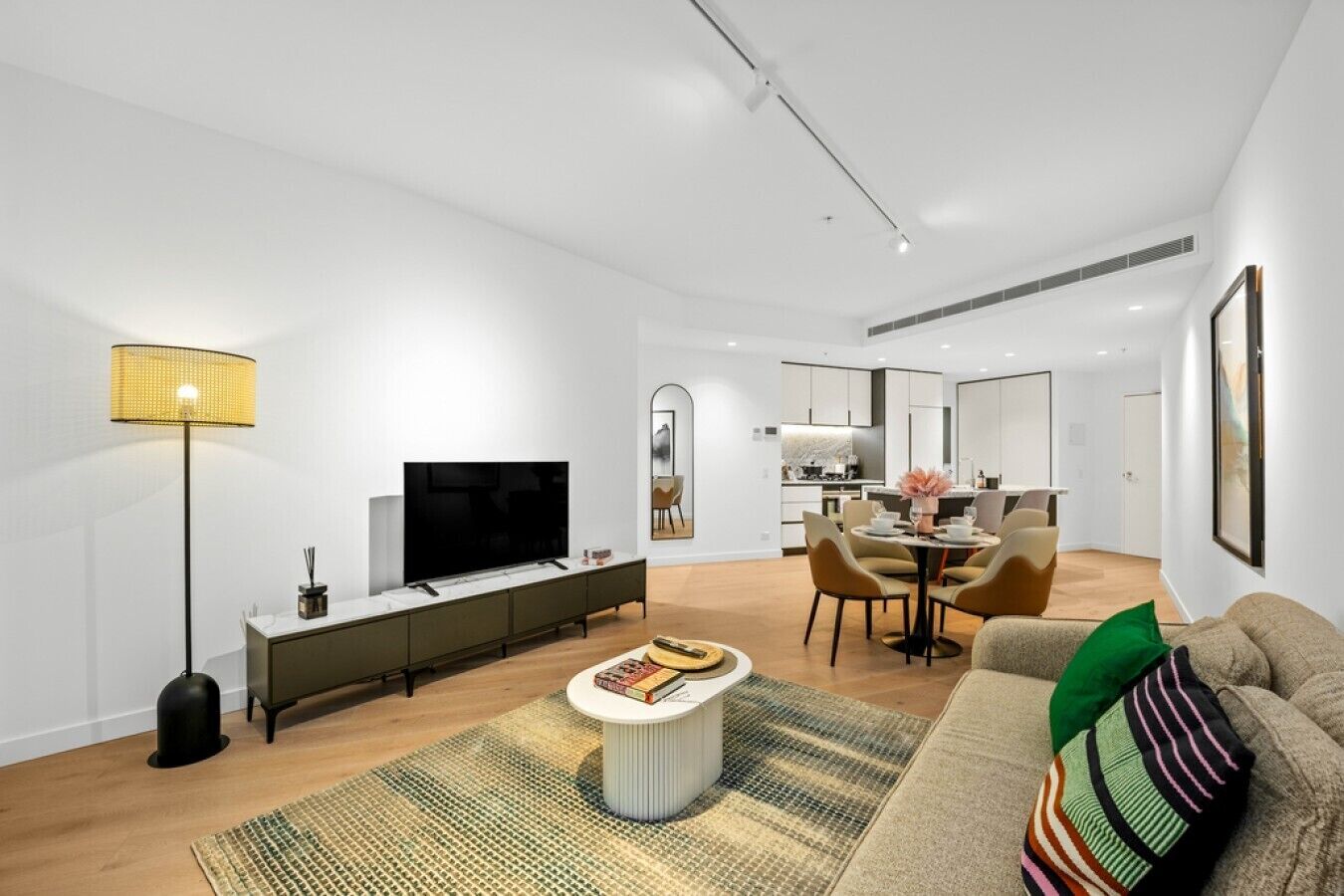 Ein modernes Wohnzimmer mit einem Flachbildfernseher, einem Essbereich mit Tisch und Stühlen sowie einer Küche im Hintergrund.
