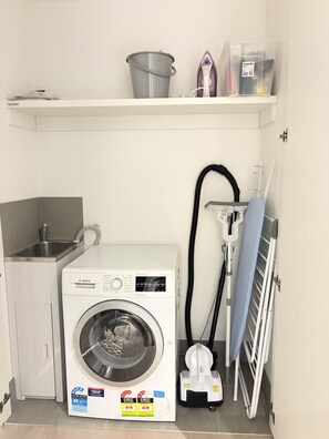 Ein kleiner Waschbereich mit einer Bosch Waschmaschine, einem Wäscheständer und einem Spülbecken.