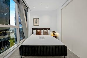 Ein modernes Hotelzimmer mit einem großen Bett, einem Nachttisch mit Lampe und einem gerahmten Bild an der Wand.