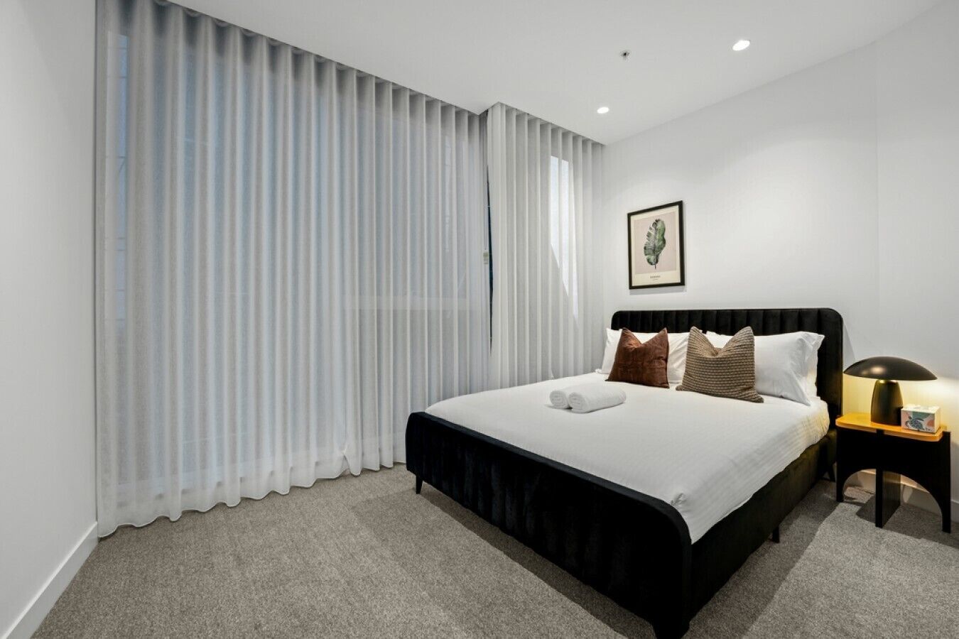 A hotel room with a bed, a nightstand, a lamp, and a framed picture on the wall.