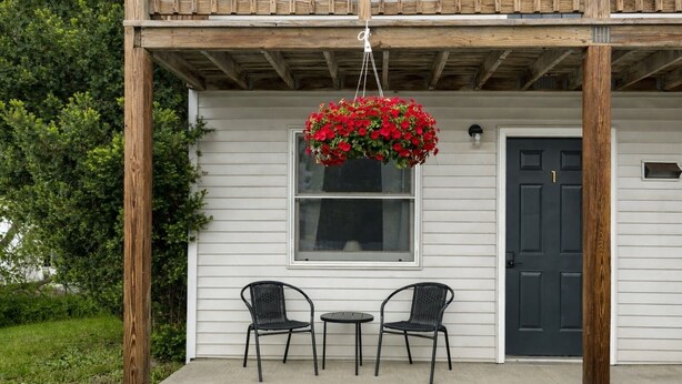Una casa con porche, dos sillas, una cesta de flores colgante y una puerta.