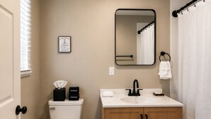 Un baño con inodoro, lavamanos, espejo y un cartel informativo enmarcado.