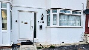 Ein weißes Wohngebäude mit Haustür, einer kleinen Veranda und einem Fenster mit dekorativer Glasverzierungen. Eine Satellitenschüssel ist ebenfalls zu sehen.