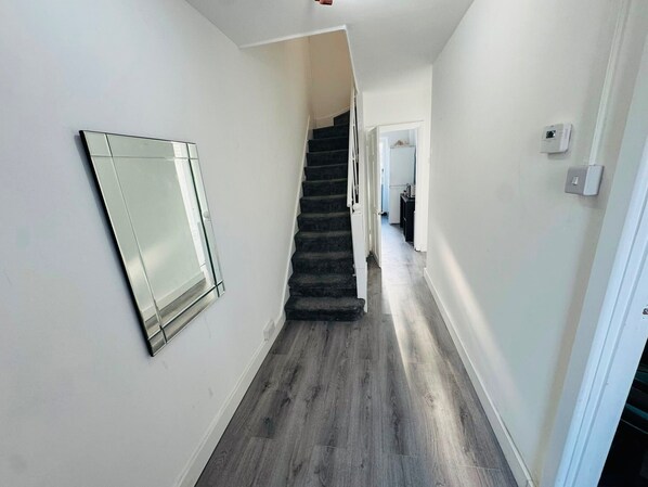 A hallway with a staircase leading to another room, a mirror on the wall, and a light switch on the wall.