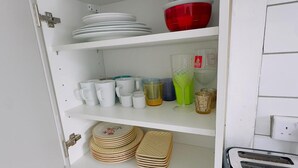 Eine Küchenschrank mit weißen Regalen, gefüllt mit verschiedenen Küchenutensilien, darunter Teller, Tassen und eine Karaffe.
