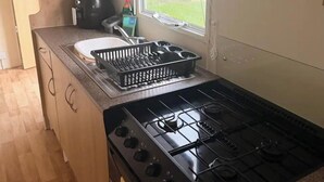 Een kleine keuken met een gasfornuis, een spoelbak en een afwasschaal.