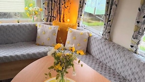 Een gezellige zithoek met een ronde tafel, een vaas met bloemen en gestreepte kussens.