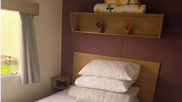 A bedroom with a bed, a headboard, a window with curtains, and a shelf with decorative items.