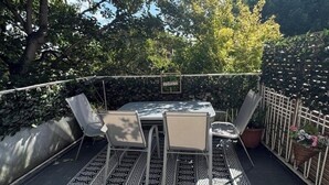 En udendørs terrasse med et bord og stole, omgivet af hegn og plantekasser.