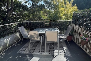 Eine Terrasse im Freien mit Tisch und Stühlen, umgeben von einem dekorativen Zaun und Topfpflanzen.