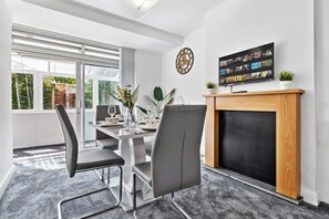 A modern dining room with a fireplace, a television mounted on the wall, and a large window. - Dartford Dream House Retreat (Dartford)